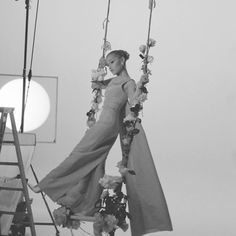 a black and white photo of a woman on a swing with flowers in her hair