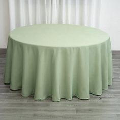 a round table with a light green cloth on it in front of a white curtain