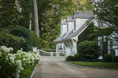 a white house surrounded by lush green trees and shrubbery with a driveway leading to it