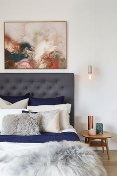 a bed with blue sheets and pillows in a bedroom next to a painting on the wall