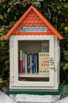 there is a little book shelf with books in it that has an orange roof on top