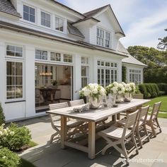 a table and chairs in front of a white house with flowers on the outside patio