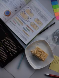 an open book next to a piece of cake on a white plate with a fork