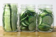 three jars filled with cucumbers sitting on top of a wooden table