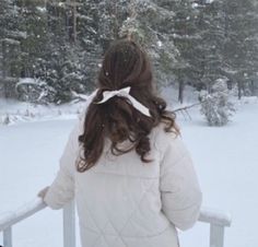 a woman in white jacket looking out over snow covered ground with trees and bushes behind her