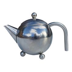 a metal tea pot with a handle on it's side and clouds in the sky