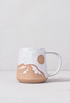 a white and brown coffee mug sitting on top of a table next to a wall