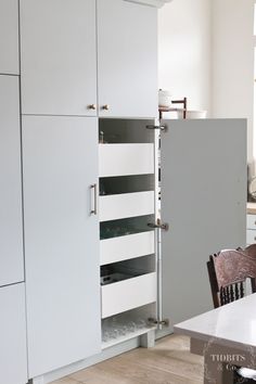 an open cabinet door in a kitchen with chairs around it and a table next to it