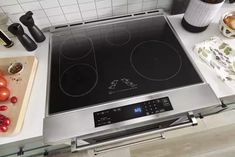 a stove top oven sitting on top of a counter next to tomatoes and other kitchen items