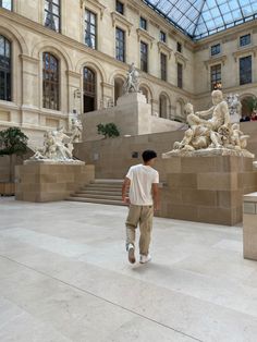 a man walking through a museum with statues on either side of the walkway and glass ceiling