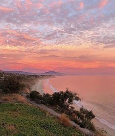 the sun is setting over the beach and ocean with hills in the distance, as seen from an overlook point