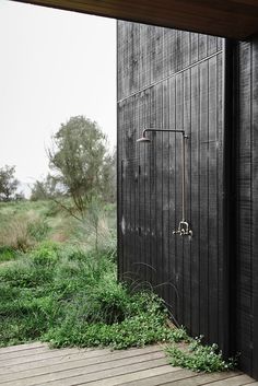 an outdoor shower in the corner of a wooden building with grass growing on the ground