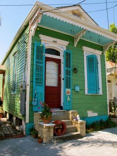 a green house with blue shutters and a red door on the front porch is shown