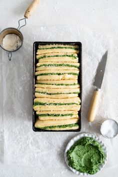 a pan filled with food next to a knife and some other items on a table