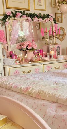 a bedroom decorated in pink and gold with flowers on the bed, dresser, mirror and chandelier