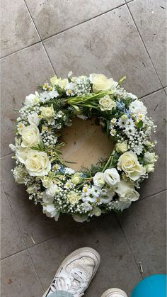 someone is standing next to a wreath on the ground with white flowers and greenery