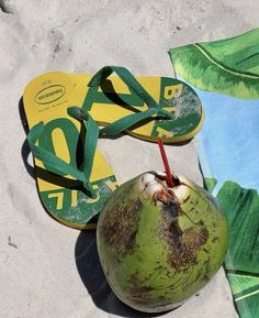 a green coconut sitting on top of a beach next to a pair of flip flops