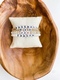 two bracelets sitting on top of a wooden bowl next to a pillow that says baseball mom and grandson