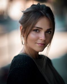 a beautiful young woman standing in front of a building with her hair pulled back and eyes closed