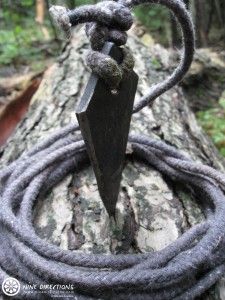 a black knife on top of a tree branch in the middle of a forest with rope wrapped around it