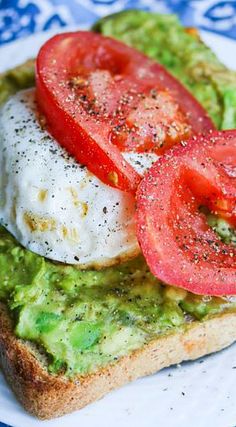 an open face sandwich topped with avocado and tomato slices on a blue and white plate