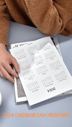 a person holding a calendar on top of a table with a cup of coffee next to it