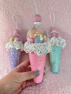 a hand holding an ice cream cone ornament in front of three other cones