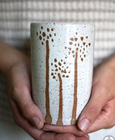 a person holding a coffee cup with trees painted on it