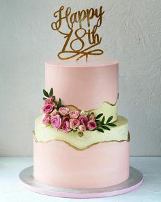 a pink and gold birthday cake with flowers on top