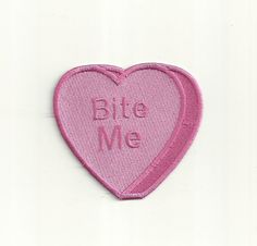 a pink heart shaped patch with the words bite me embroidered on it's side