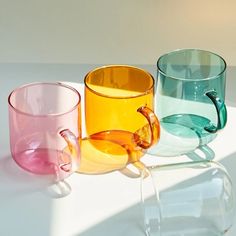 three different colored glass cups sitting next to each other on a white counter top,