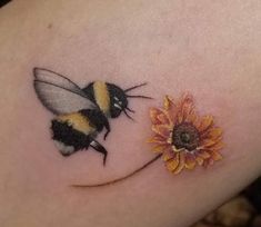 a bee and flower tattoo on the back of a woman's arm, with one being held in place