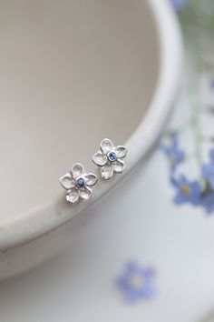 Sweet Little Solid Silver Forget-Me-Not Earrings. With beautiful Cornflower Blue Sapphire centres. Adding that gorgeous touch of blue.  The forget-me-not flowers hold meaning for me personally as the icon for The Alzheimers Society here in the UK. They flower late April, early May which is just gorgeous as we leave those dreary winter months. These dainty little stud earrings have been lovingly carved from a piece of wax and cast into these beautiful solid silver earrings. I included a special star on the rear of the flowers to echo the little star at their centres. The silver flower itself is recycled silver and fitted with the sterling 925 posts and butterflies. Each flower measure approx 8mm. These earrings can be personalised with birthstones etc should you wish. Blue Flower Stud Earrings, Earrings Studs Silver, Blue And Silver Earrings, Pretty Stud Earrings, Forget Me Not Jewelry Sterling Silver, Little Earrings, Flower Earrings Silver, Forget Me Not Earrings, Flower Stud Earrings