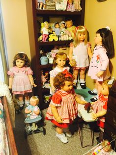 a group of dolls that are standing in front of a bookshelf filled with children's toys