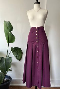 This gorgeous vintage 80s skirt is ultra high-waisted and has an intricate waistline with big bold gold buttons that go all the way down  It is in a lovely deep rich purple.  ~ Gorgeous pleats  ~ There is no stretch at all, so please see the measurements  ~ Perfect vintage condition  ~ Gorgeous detailed gold buttons ~ It has loops for a belt ~ It is made out of polyester and viscous material however, the feel is like a thick cotton ~ Since it is a thicker material, the skirt holds its shape very 80s Skirts, 80s Skirt, Purple Skirt, Rich Purple, Vintage Rock, Royal Purple, Circle Skirt, Drop Waist, Gold Buttons