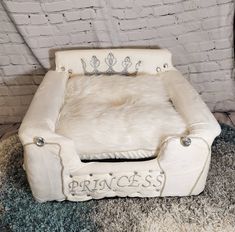 a white dog bed with princess written on the front and back, sitting on a shaggy rug