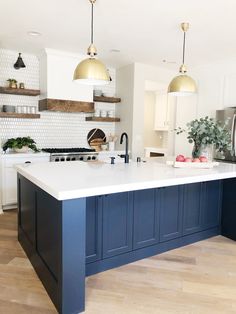 a large kitchen with blue cabinets and white counter tops, gold pendant lights over the island