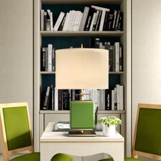 a green lamp sitting on top of a table next to two chairs and a book shelf