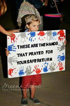 a young boy holding a sign that says, these are the hands that pray for your safe return