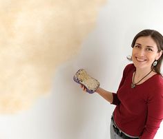 a woman holding a paint roller in front of a wall