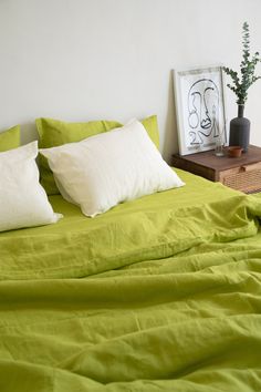 a bed with green sheets and pillows on top of it next to a wooden nightstand