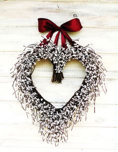 a heart shaped wreath hanging on the side of a white wall with a red bow