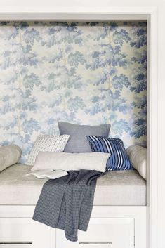 a white bench with pillows on it in front of a floral wallpapered wall