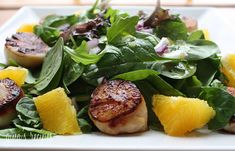 a white plate topped with spinach and scallops next to lemon wedges