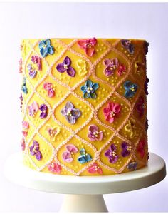 there is a yellow cake with flowers on the top and bottom layer, decorated with crochet