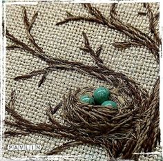 three green eggs in a nest on top of burlocked fabric with brown stems