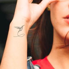 a woman with a small humming tattoo on her left arm and right hand behind her ear