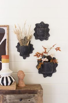 three black and white vases with flowers in them on a table next to a wall