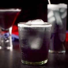 two glasses filled with liquid and ice sitting on a table next to each other,