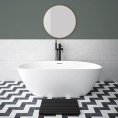 a white bath tub sitting on top of a black and white tiled floor next to a round mirror